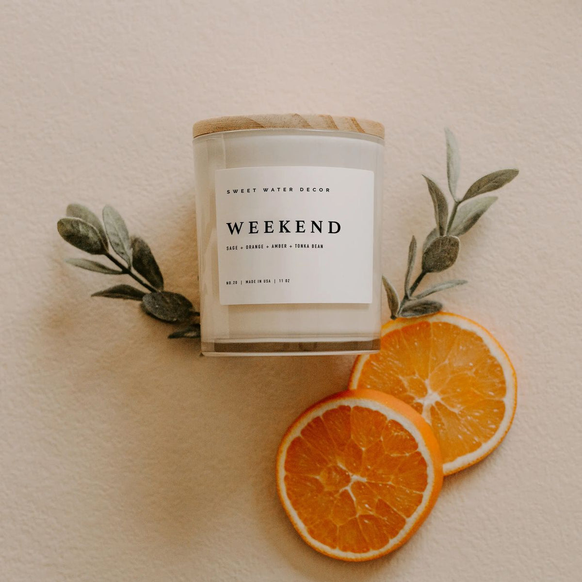 Candle labeled 'Weekend' with sliced oranges and leaves on a neutral background