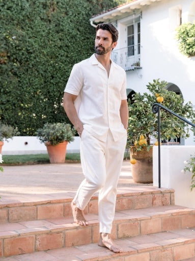 Man in a white outfit standing on steps outside a house