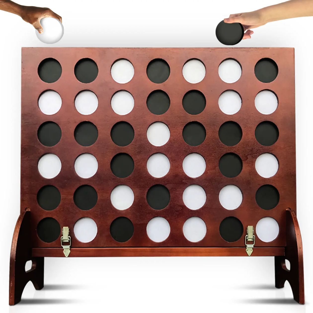 A wooden Connect-Five style game board with circular black and white discs, shown on a white background with two hands reaching in from the top to drop new discs.