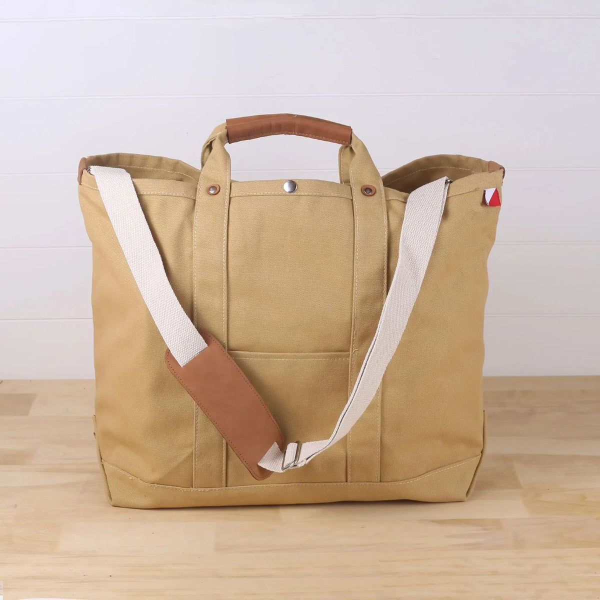 Beige tote bag with brown handle and strap on a wooden surface