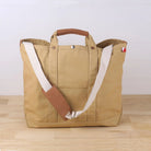 Beige tote bag with brown handle and strap on a wooden surface